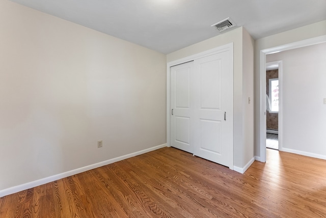 unfurnished bedroom with a baseboard heating unit, wood-type flooring, and a closet