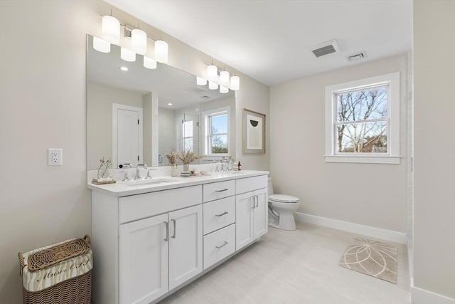 bathroom featuring double vanity, toilet, baseboards, and a sink