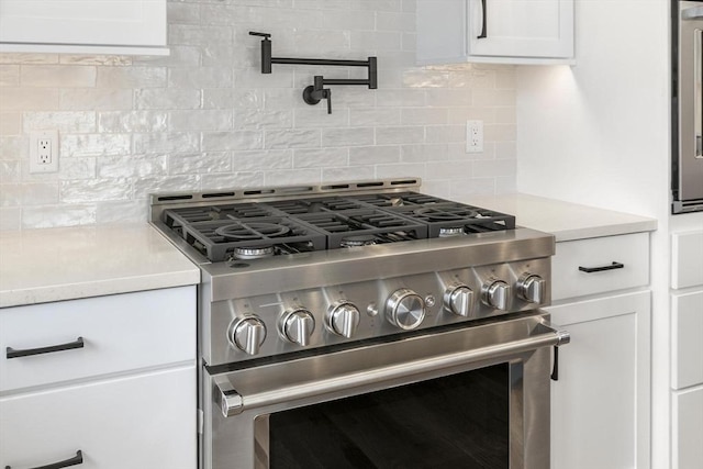 kitchen with tasteful backsplash, white cabinets, stainless steel range, and light countertops