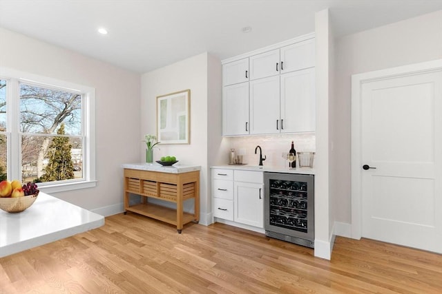 bar with indoor wet bar, wine cooler, tasteful backsplash, and light wood-style flooring