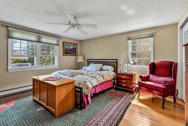 25 Pheasant Cove Cir, Yarmouth, MA 02675 - bedroom with multiple windows, light wood finished floors, a textured ceiling, a baseboard heating unit, and a ceiling fan