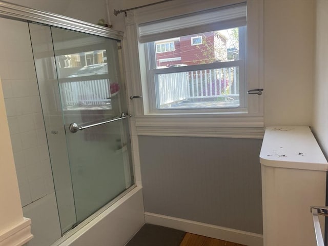bathroom featuring shower / bath combination with glass door and baseboards