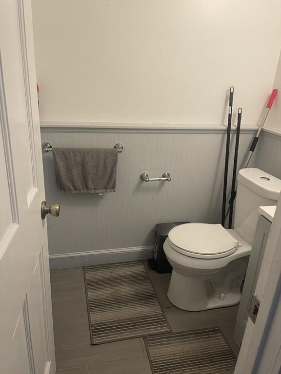 half bathroom with baseboards, a wainscoted wall, and toilet