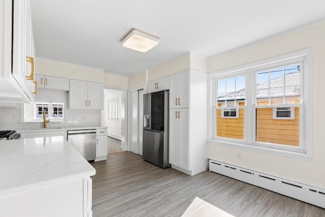 kitchen featuring tasteful backsplash, a baseboard heating unit, stainless steel appliances, light stone countertops, and white cabinets