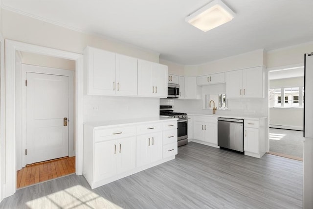 kitchen featuring appliances with stainless steel finishes, sink, white cabinets, a baseboard heating unit, and light hardwood / wood-style flooring