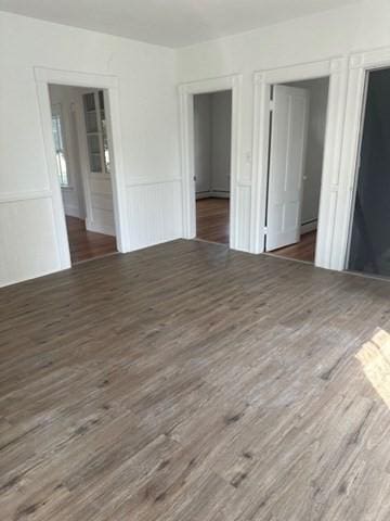 678 School St, Webster, MA 01570 - unfurnished bedroom with wood finished floors, a baseboard heating unit, and a wainscoted wall