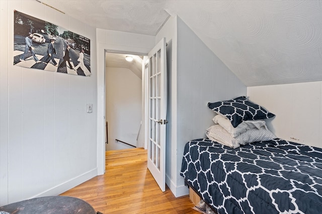 bedroom featuring vaulted ceiling, hardwood / wood-style floors, and a textured ceiling