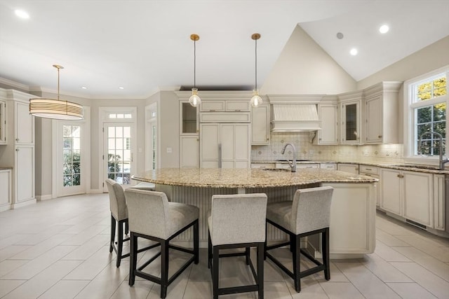 kitchen with sink, light stone countertops, a center island with sink, decorative light fixtures, and custom exhaust hood