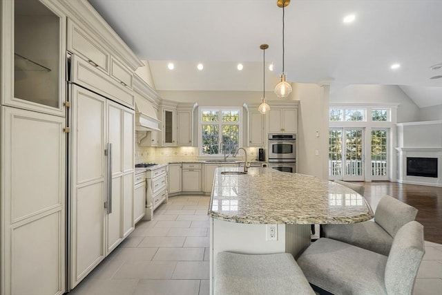 kitchen with pendant lighting, a kitchen breakfast bar, an island with sink, decorative backsplash, and vaulted ceiling