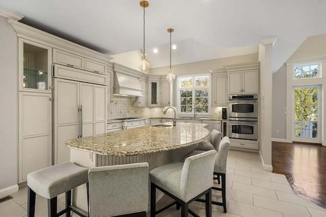 kitchen with custom range hood, sink, stainless steel appliances, and an island with sink