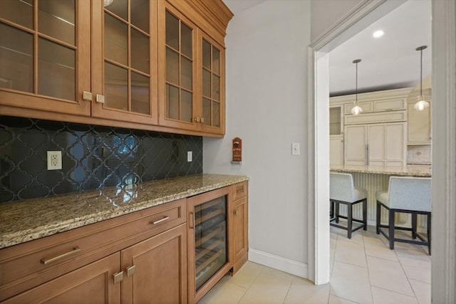 kitchen featuring decorative light fixtures, backsplash, beverage cooler, light tile patterned floors, and light stone countertops