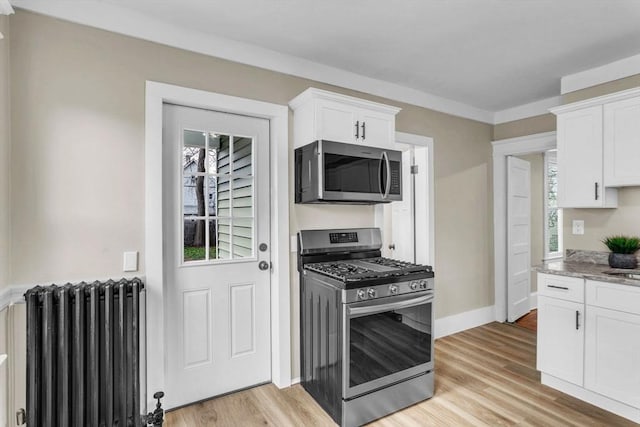 kitchen with white cabinets, radiator heating unit, light wood-type flooring, and appliances with stainless steel finishes