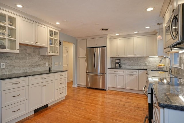 kitchen with light wood-style flooring, decorative light fixtures, stainless steel appliances, white cabinets, and glass insert cabinets