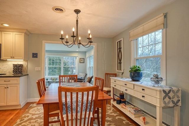 dining area featuring a wealth of natural light, visible vents, light wood finished floors, and an inviting chandelier