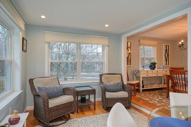 living area with a healthy amount of sunlight, light wood-type flooring, a chandelier, and baseboards