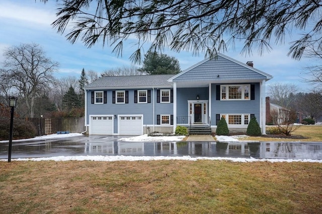 raised ranch with a garage, a chimney, a front lawn, and aphalt driveway