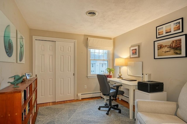 office with visible vents, a baseboard heating unit, and wood finished floors