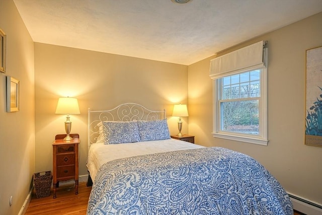 bedroom with baseboard heating, wood finished floors, and baseboards