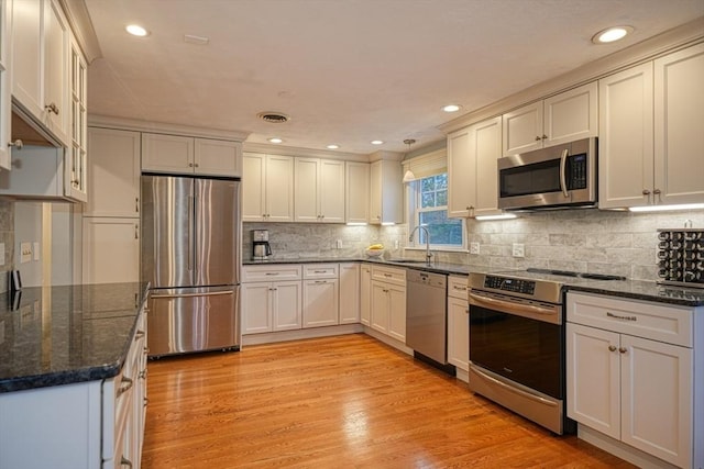 kitchen featuring stainless steel appliances, visible vents, light wood-style floors, a sink, and dark stone counters