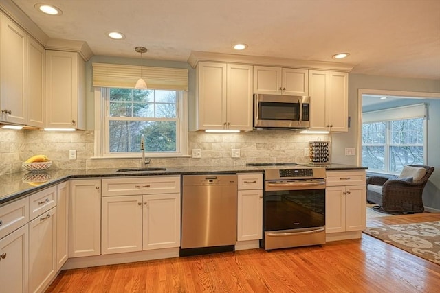 kitchen with decorative backsplash, light wood-style flooring, appliances with stainless steel finishes, pendant lighting, and a sink