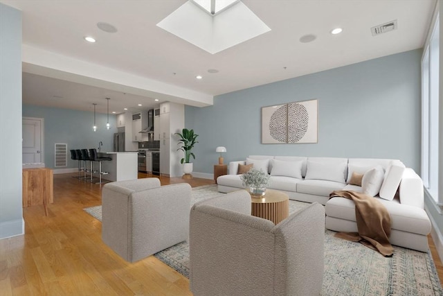 living area featuring baseboards, light wood-style flooring, recessed lighting, and a skylight