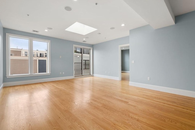 unfurnished living room featuring a skylight, light wood-style flooring, baseboards, and recessed lighting