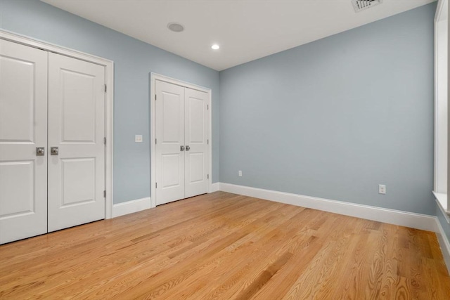 unfurnished bedroom featuring multiple closets, light wood finished floors, baseboards, and recessed lighting