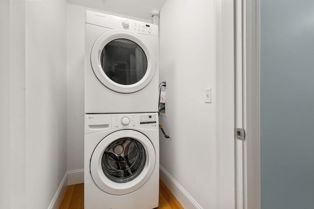 washroom featuring estacked washer and dryer, wood finished floors, and baseboards