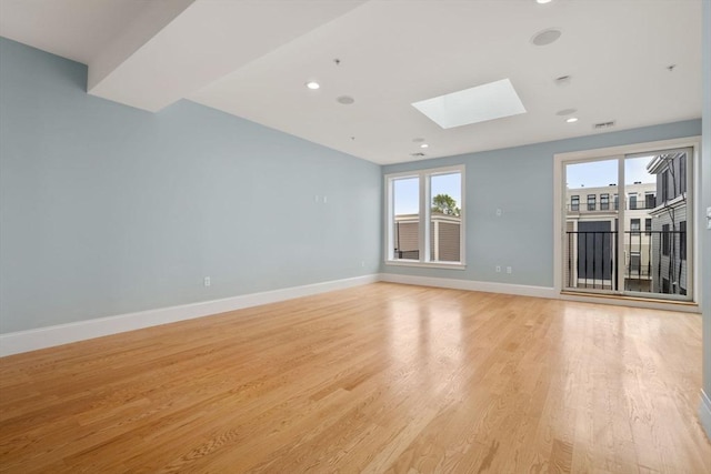 unfurnished room featuring a skylight, light wood finished floors, baseboards, and recessed lighting
