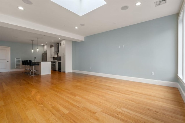unfurnished living room featuring light wood-type flooring, baseboards, recessed lighting, and a skylight