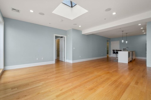 unfurnished living room featuring a skylight, light wood finished floors, baseboards, and recessed lighting