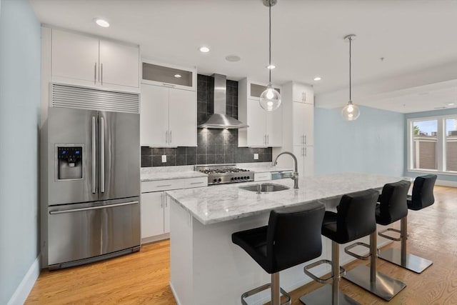 kitchen featuring stainless steel fridge with ice dispenser, wall chimney range hood, a sink, stove, and light wood finished floors