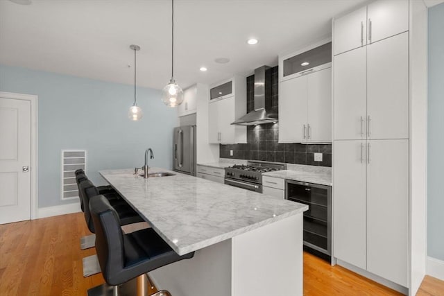 kitchen with wall chimney exhaust hood, a sink, high end appliances, wine cooler, and a breakfast bar area