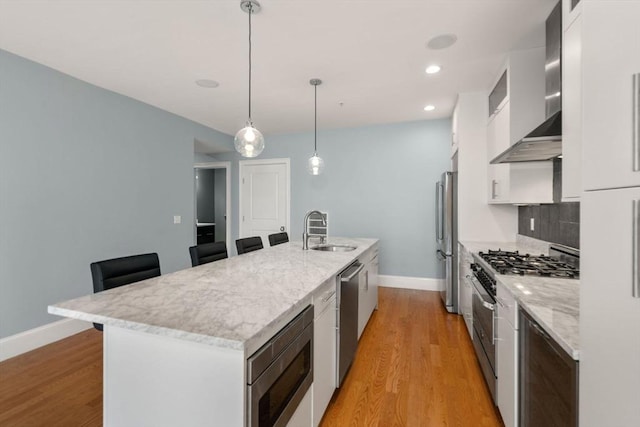 kitchen with a sink, stainless steel appliances, baseboards, a kitchen island with sink, and white cabinetry