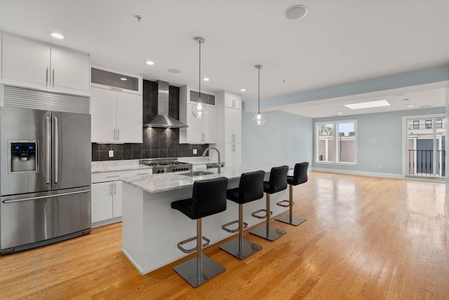 kitchen with stainless steel refrigerator with ice dispenser, a sink, wall chimney range hood, tasteful backsplash, and a breakfast bar area