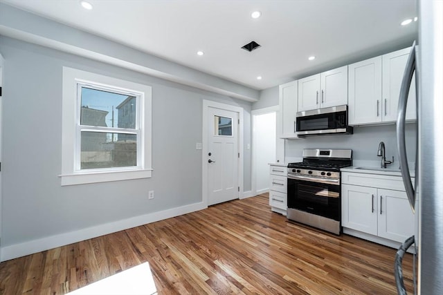 kitchen featuring recessed lighting, appliances with stainless steel finishes, white cabinetry, a sink, and wood finished floors