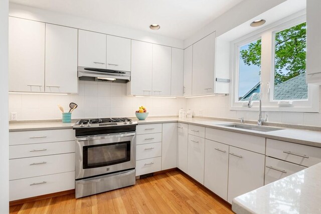 kitchen with a sink, extractor fan, stainless steel gas stove, light countertops, and white cabinets