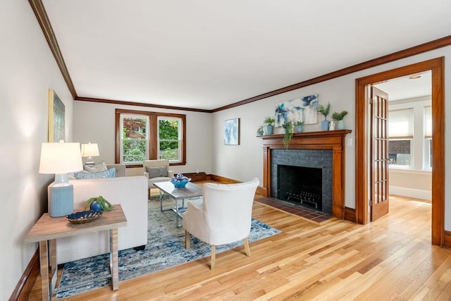 living room with light wood finished floors, ornamental molding, a brick fireplace, and baseboards