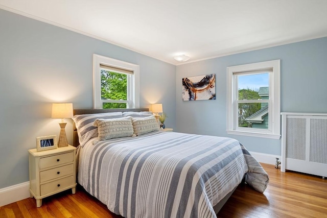 bedroom with ornamental molding, radiator, baseboards, and wood finished floors
