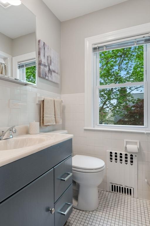bathroom with toilet, radiator, tile walls, tile patterned flooring, and vanity