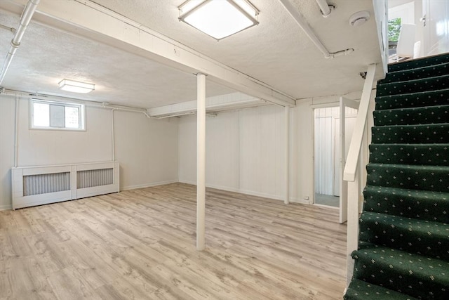 below grade area with baseboards, stairs, radiator heating unit, and wood finished floors