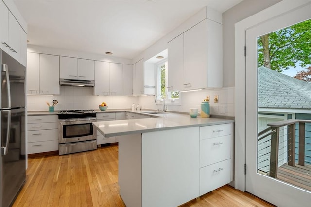 kitchen featuring a peninsula, a sink, freestanding refrigerator, under cabinet range hood, and gas stove