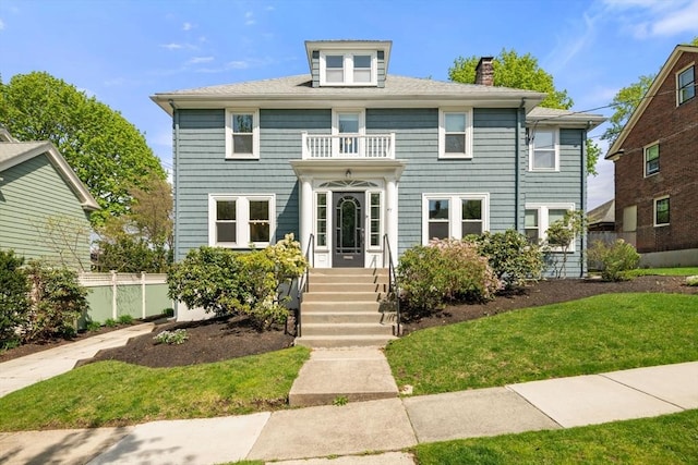 view of front of house with fence, a front lawn, a chimney, and a balcony