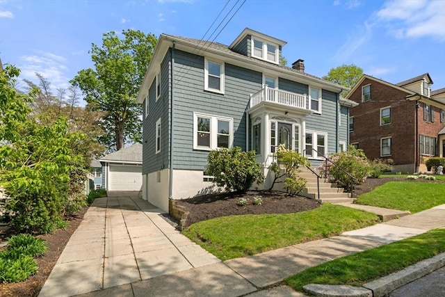 traditional style home featuring a balcony, a front yard, a chimney, and a detached garage
