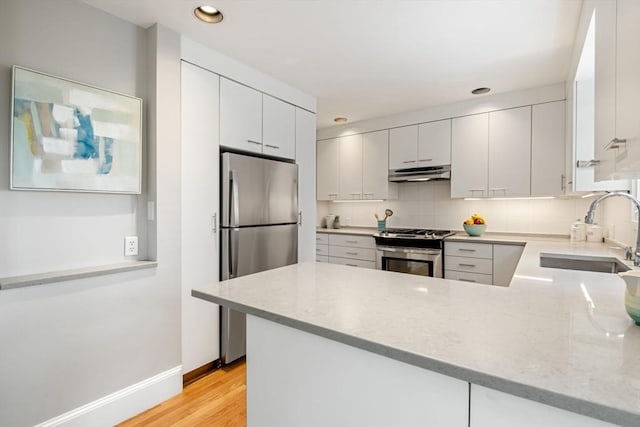 kitchen with a sink, a peninsula, recessed lighting, under cabinet range hood, and appliances with stainless steel finishes