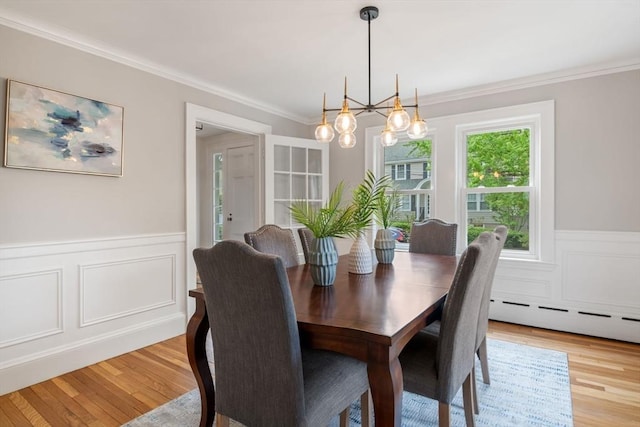 dining area featuring a baseboard heating unit, ornamental molding, an inviting chandelier, wainscoting, and light wood-type flooring