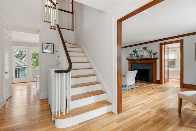 stairs with ornamental molding, wood finished floors, baseboards, and a brick fireplace