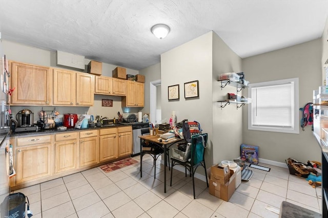 kitchen featuring light brown cabinetry, dark countertops, stainless steel dishwasher, a sink, and light tile patterned flooring