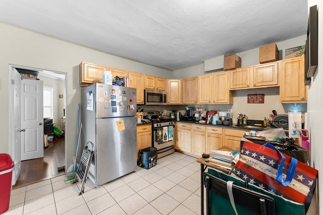 kitchen featuring light tile patterned flooring, dark countertops, stainless steel appliances, and light brown cabinetry