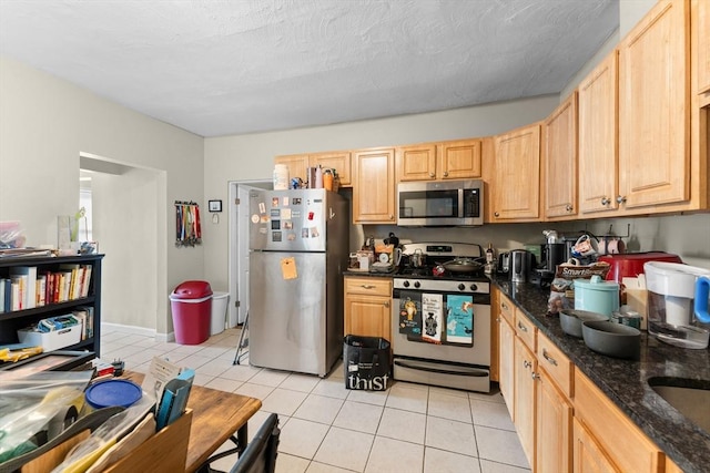 kitchen featuring light brown cabinets, dark stone countertops, stainless steel appliances, and light tile patterned floors